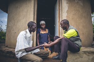 FH Uganda staff member praying with two village members outside their dirt home