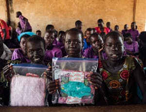 Girls in Uganda hold up women's hygiene kits