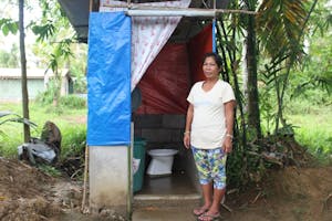 Woman in Philippines stands next to her latrine