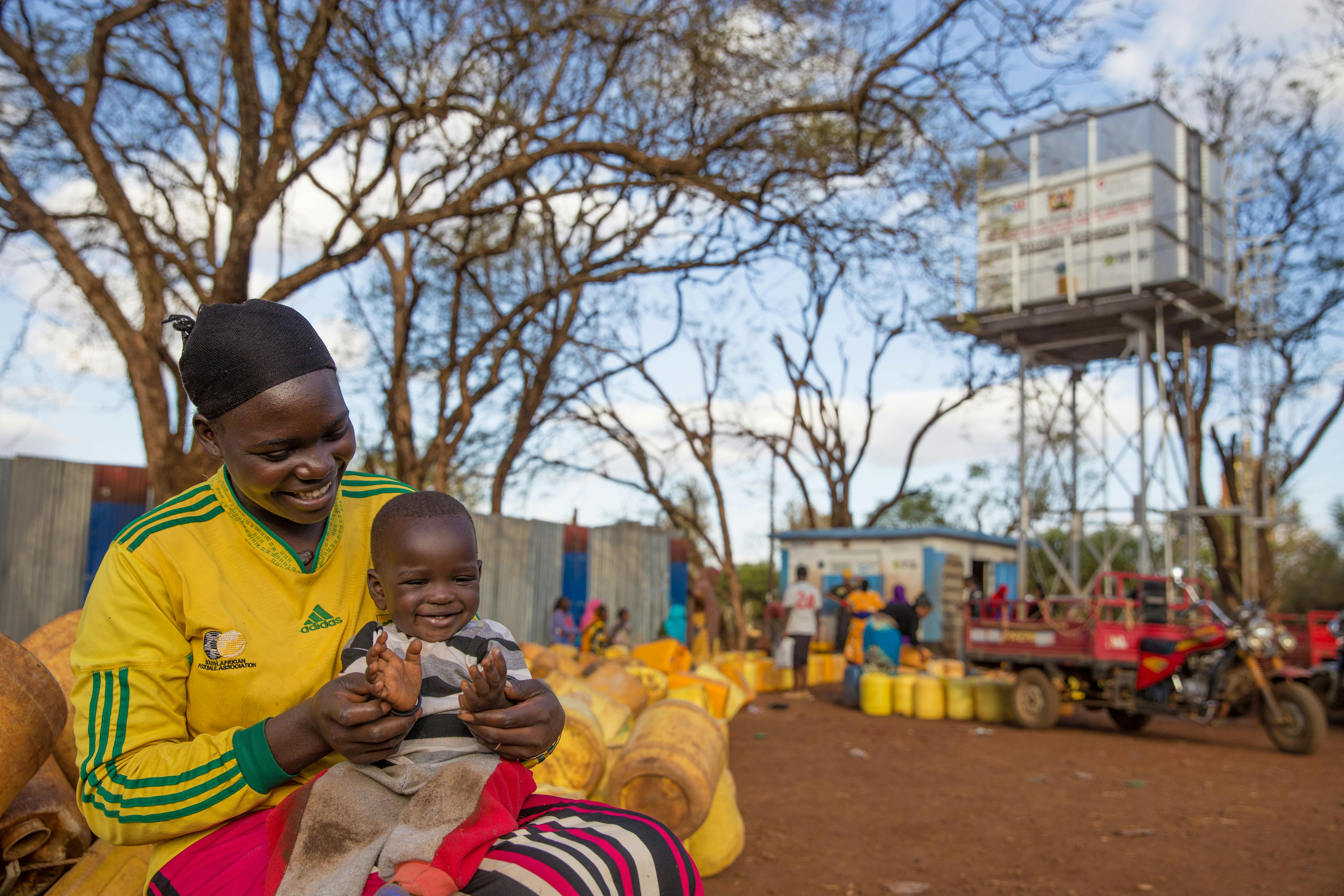 A woman holds her baby boy, in front of an innovative kiosk bring clean water in Kenya