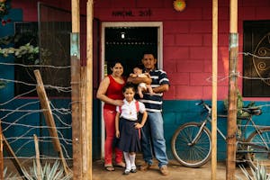 Family of four stands outside their red and blue brick house in Nicaragua