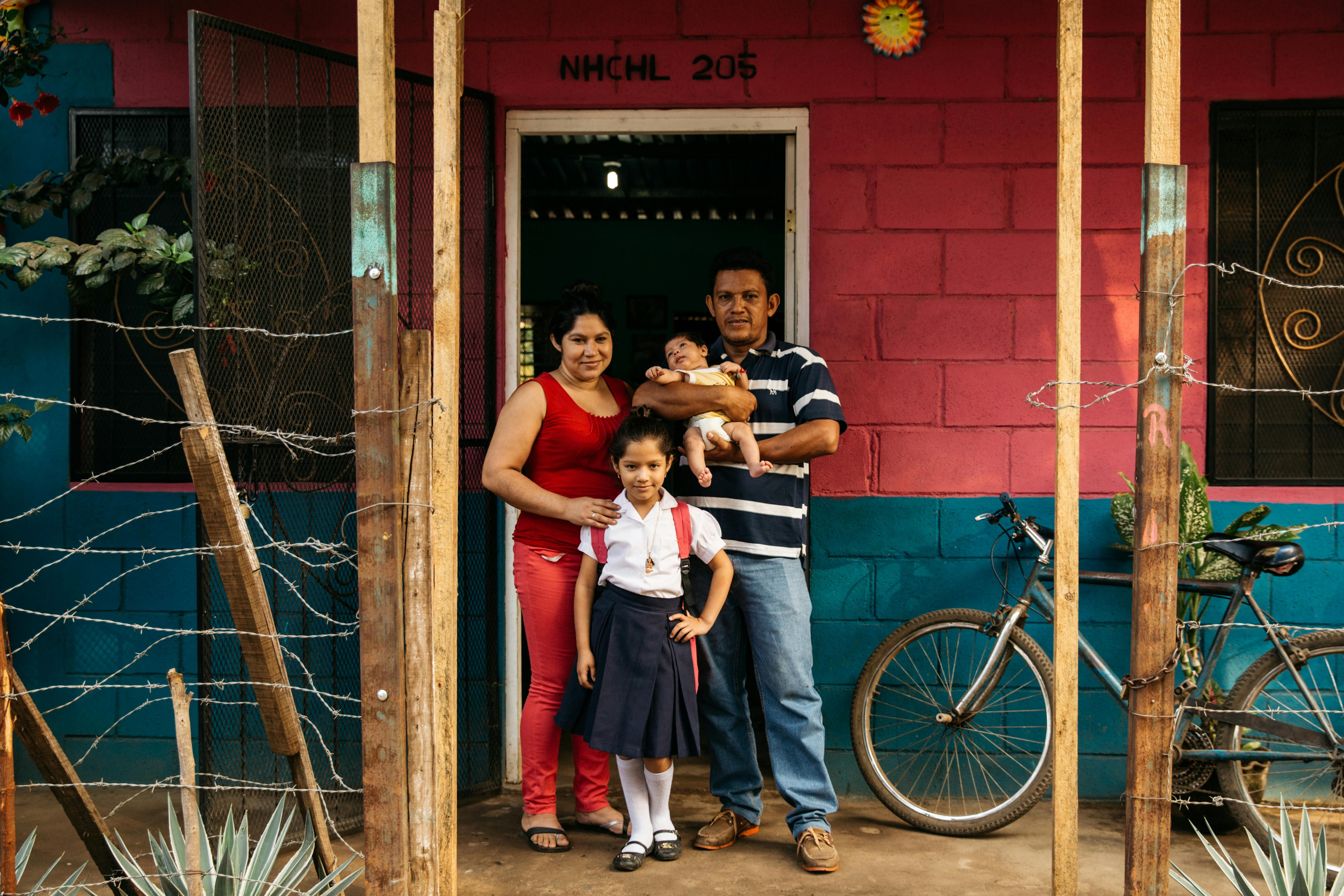 International Womens Day Photoessay - Family of four stands outside their red and blue brick house in Nicaragua 