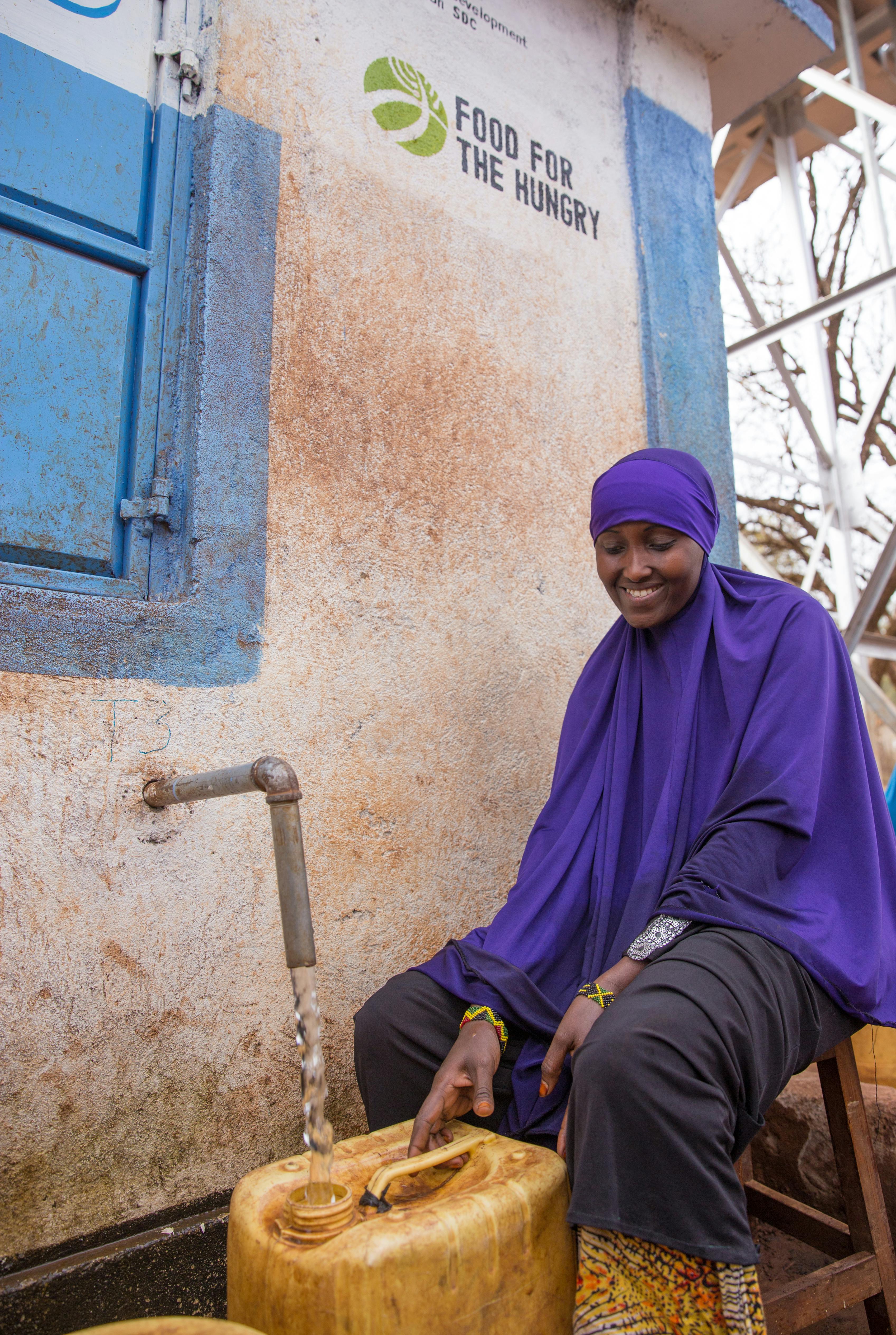 Kenyan woman in purple clothing gathers clean water from kiosk