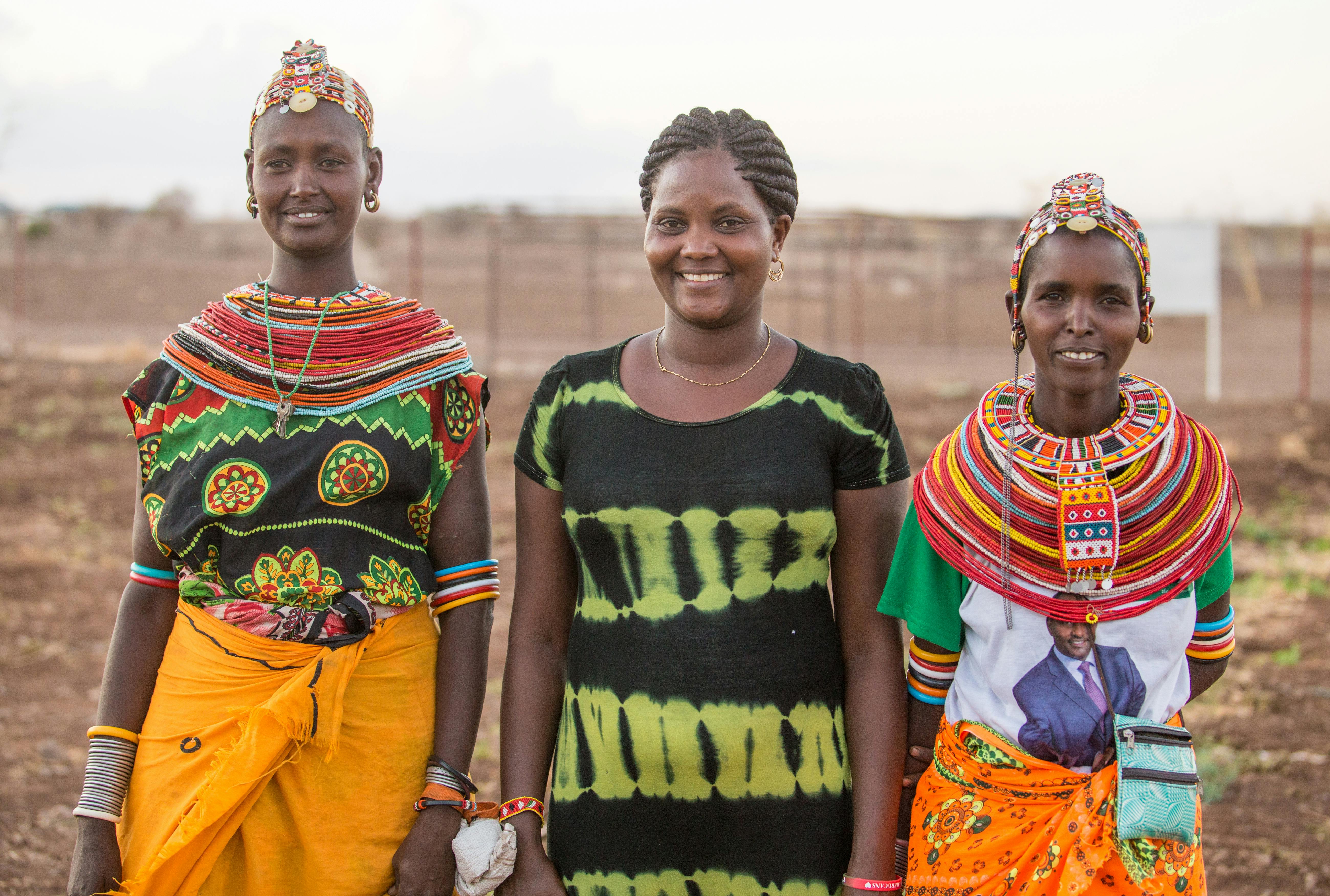 International Womens Day Photoessay - Three Kenyan women holding hands in traditional culture outfits and attire, with beaded necklaces and headbands
