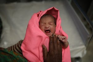 Crying newborn baby in pink blanket