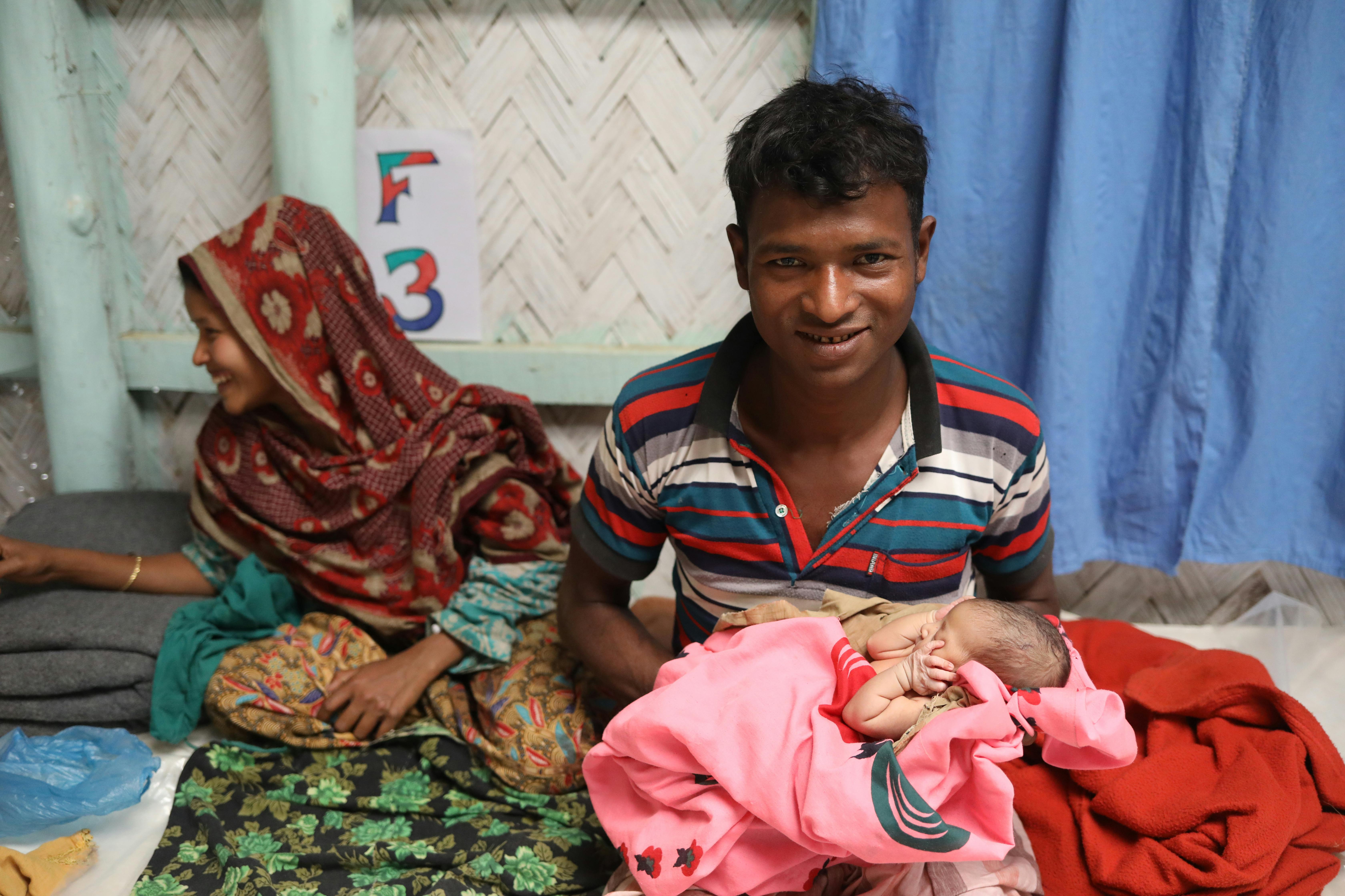 Mother in sari next to husband holding newborn baby wrapped in pink blanket