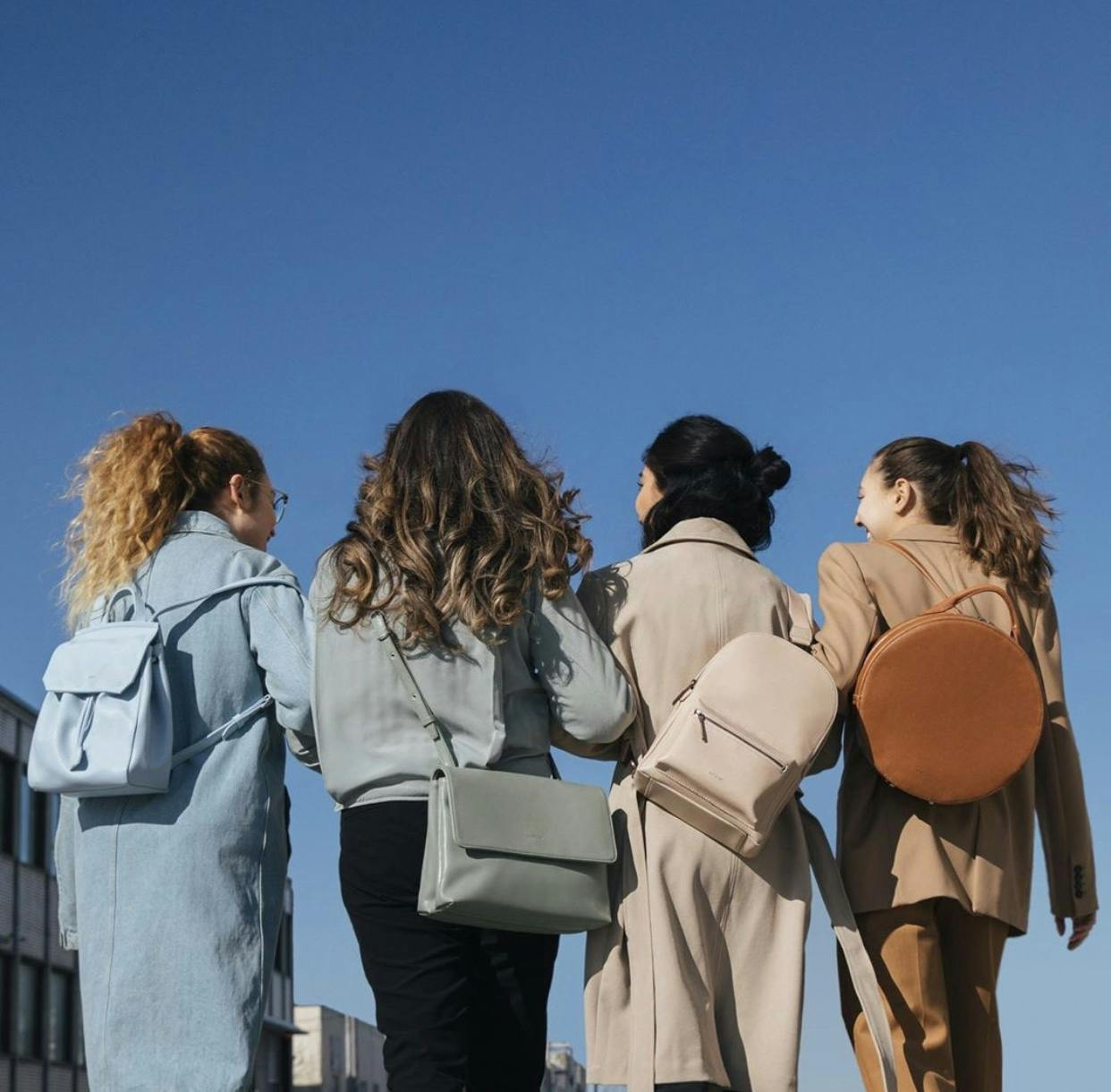 Four women standing with their back to us, wearing coordinating backpacks and purses from sustainable brands