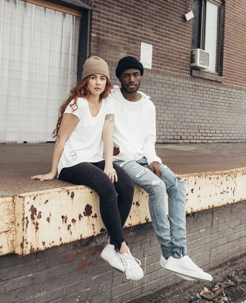 woman and man sitting on the side of a building wearing sustainable clothing brands