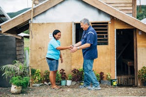 CEO/President Gary Edmonds shakes the hand of a woman outside a wooden house in the Philippines