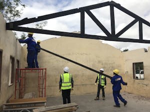 Men installing beams to hold a new tin roof on cement block school building