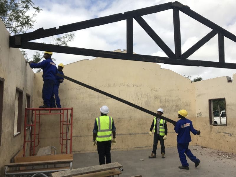 Men installing beams to hold a new tin roof on cement block school building