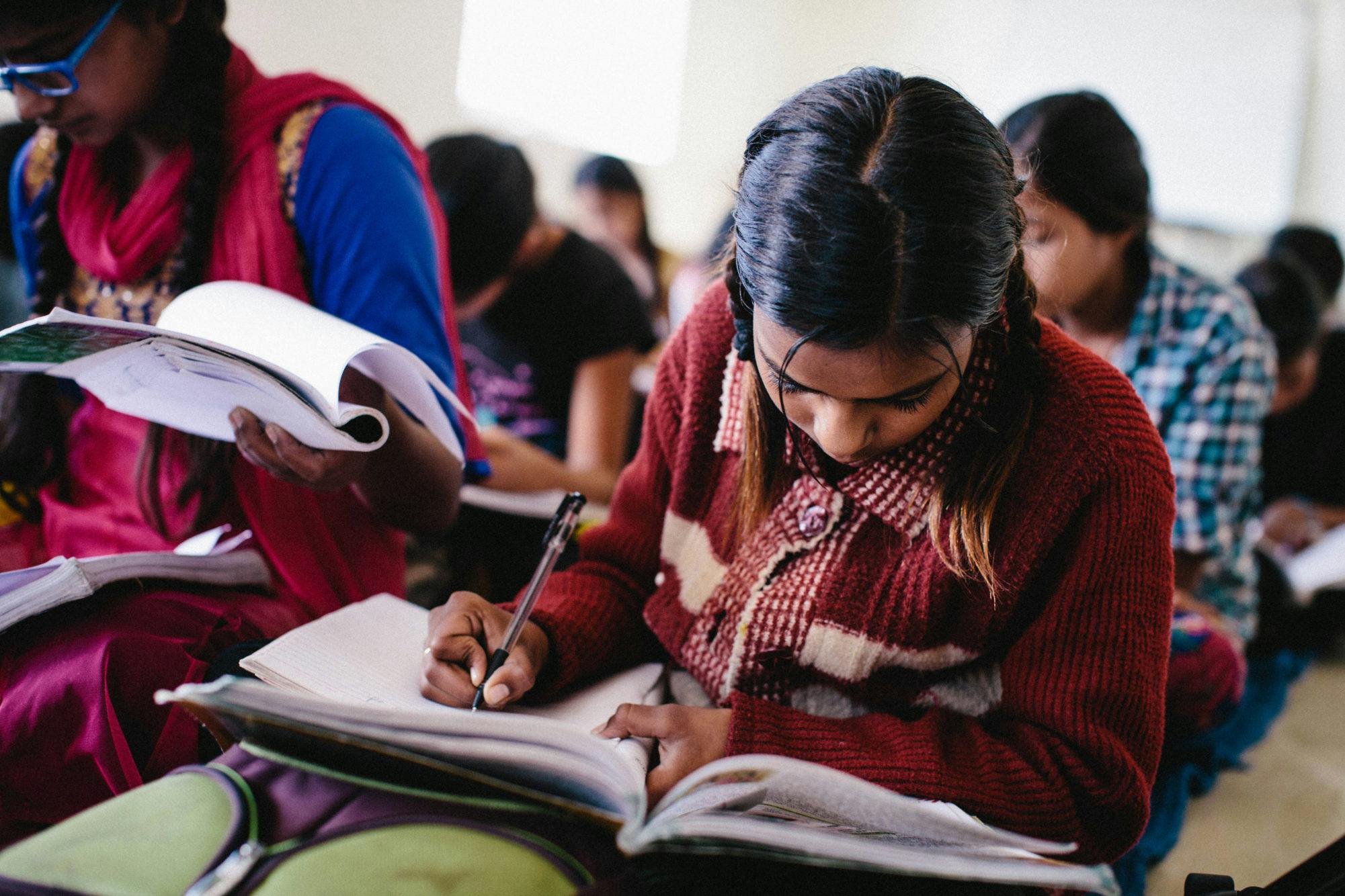School girl in India wearing a red coat focuses on her studies and looks down at book