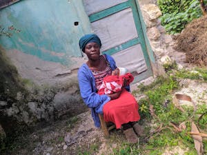 Farah, Haitian woman in a red dress holding her baby, looks at the camer