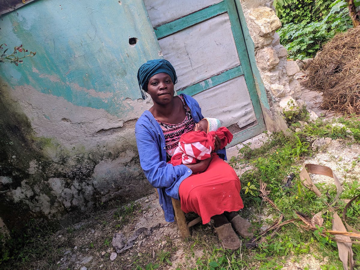Farah, Haitian woman in a red dress holding her baby, tells FH about her struggles providing since the hunger crisis started in Haiti.