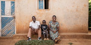Happy family of father, mother, and son sit outside their house in Burundi, smiling after being healed from deworming treatments.