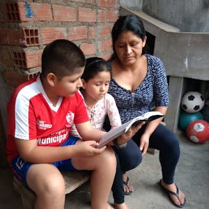 Youth in Peru learns to value a children's Bible given to him by Food for the Hungry and sits on a brick ledge reading with his sister and mother.