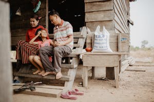 Cambodian family outside their house on wooden beams. Girl sits in lap of father and mother