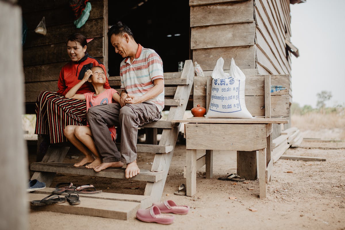 Cambodian family outside their house on wooden beams. Girl sits in lap of father and mother