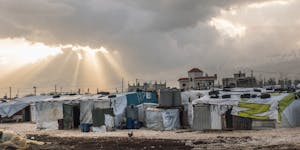 Landscape photo of gray rain clouds and light peaking through over a gray Syrian refugee camp in Lebanon, where FH is responding.
