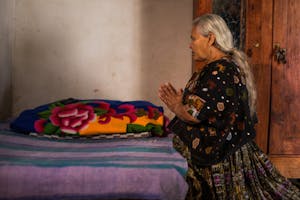 Guatemalan elderly woman prays and kneels by her bed