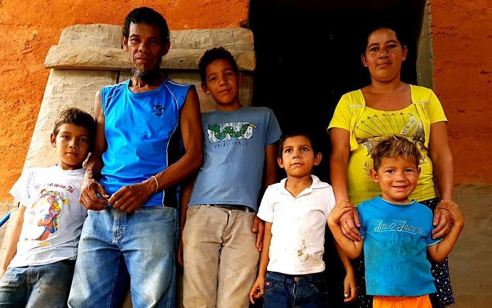 Nicaraguan farmer stands outside an orange house with his wife and four kids.