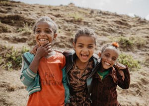 Three girls smile for the camera hugging in Ethiopia