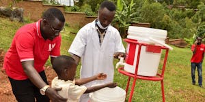 two men helping a child wash his hands at a health center