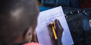 Closeup of boy in Haiti in a red polo writing in a notebook