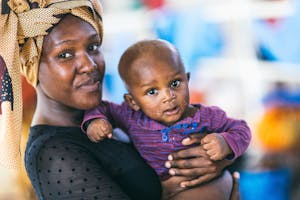 Mother in Mozambique with headscarf holds her baby in a purple shirt