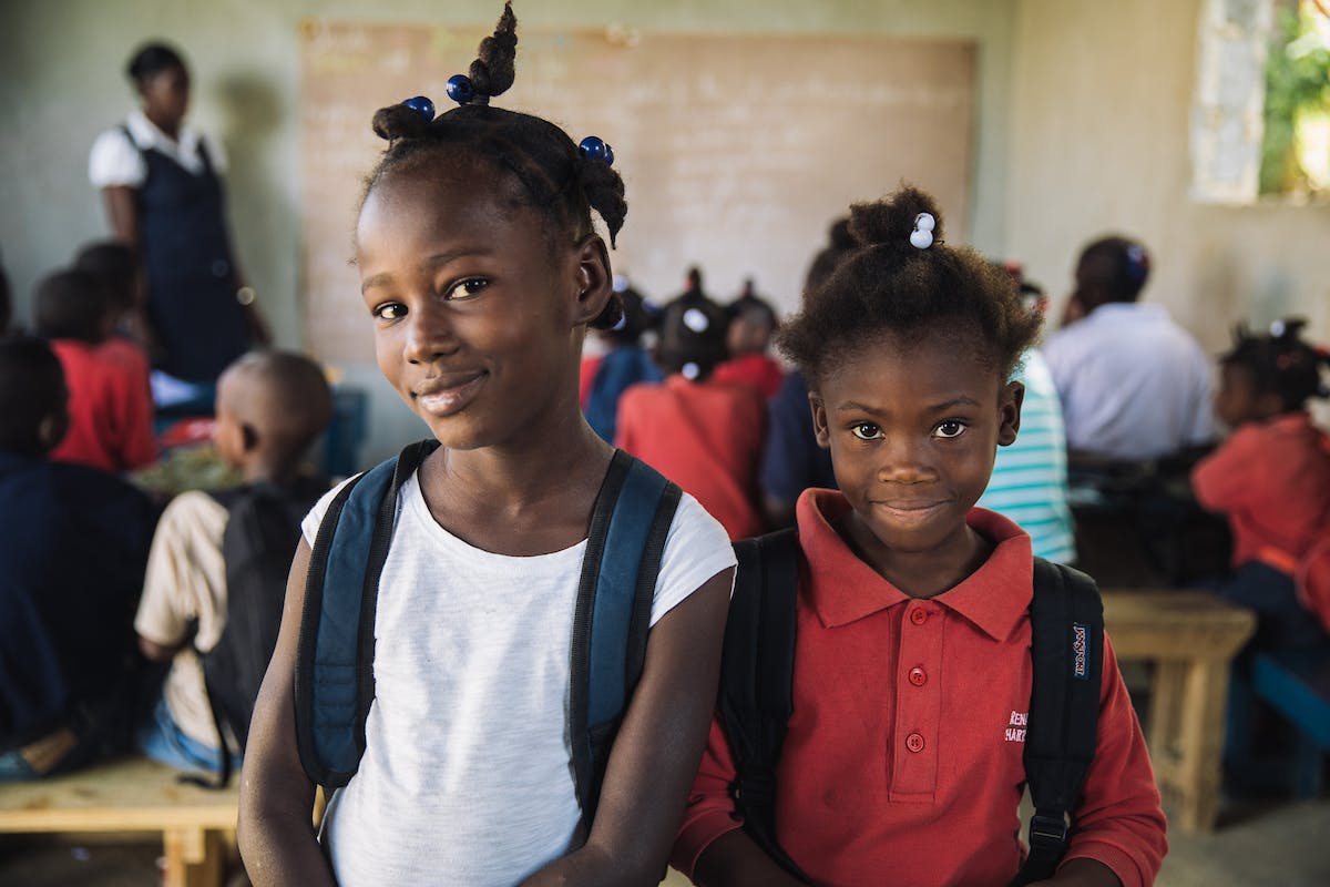 Two girls elementary school aged wearing white and red shirts inside Haitian classroom