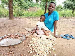 woman with young baby sitting on the ground with shea nuts
