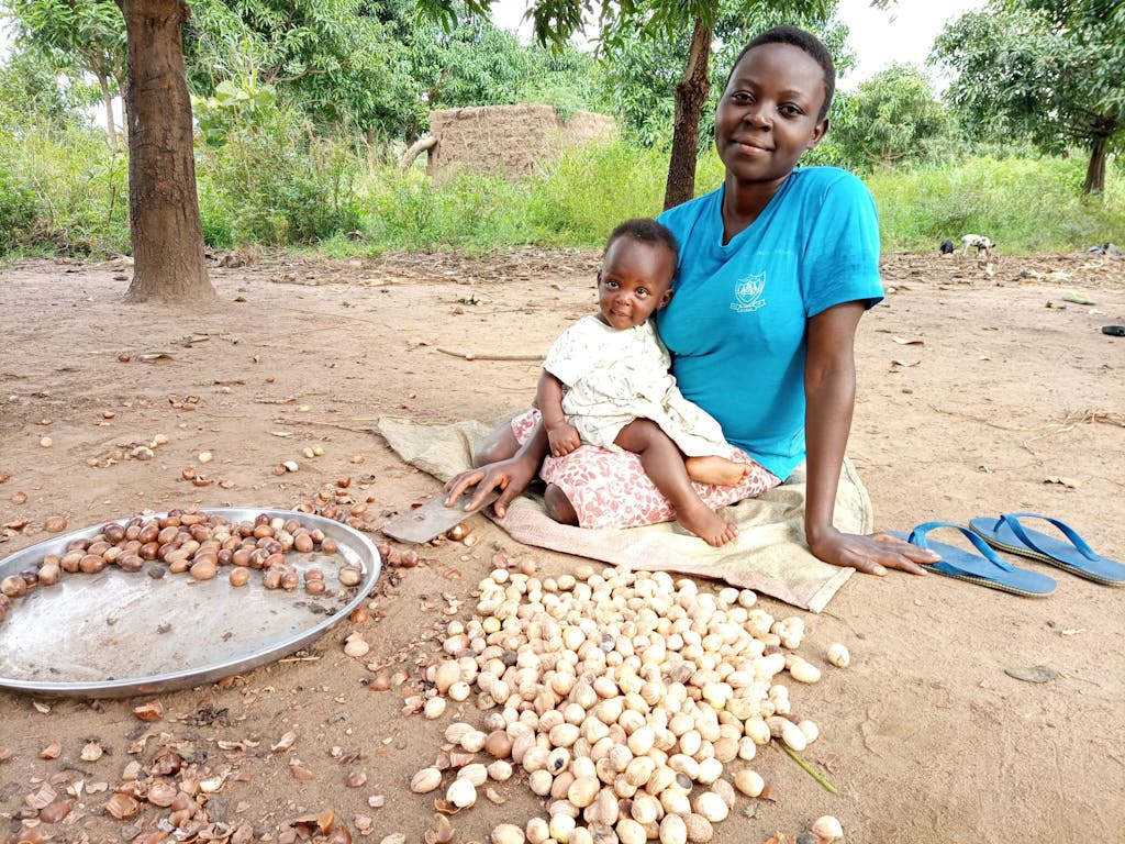 woman with young baby sitting on the ground with shea nuts
