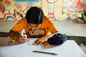 boy in orange shirt writing letter