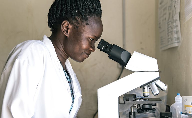Ugandan health professional woman in white coat looking into laboratory microscope