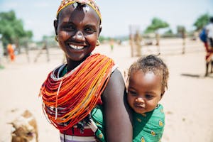 kenyan woman in bright red and yellow neckpiece with baby on her back