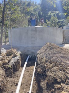 Circular cement tank on top of hill with two pipes leading out of the bottom of the tank
