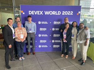 8 FH staff standing in front of cobranded display with Devex Word and FH logos