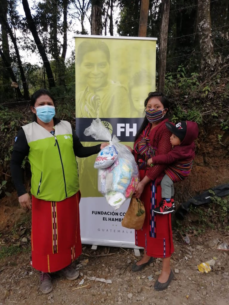 two women in front of FH sign with one woman carrying relief supplies