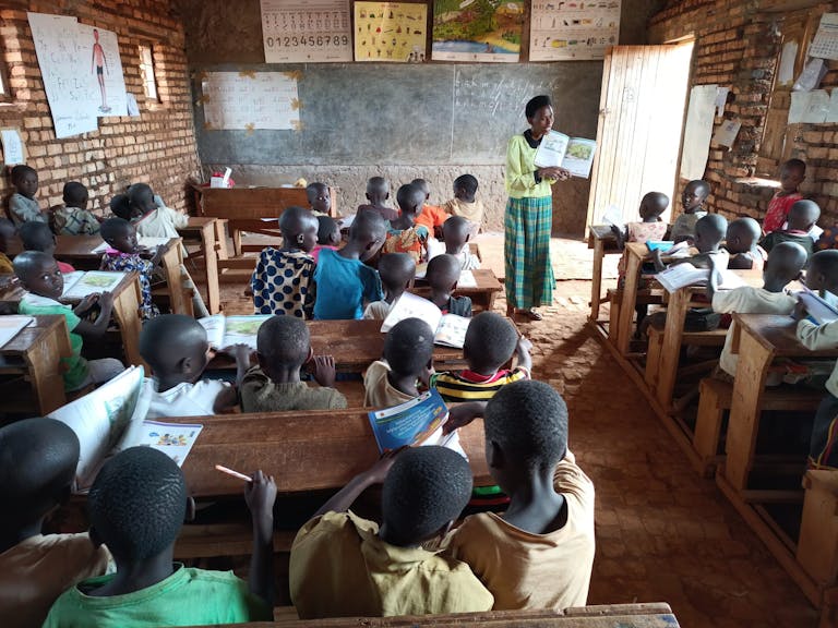 teacher in classroom in Burundi standing in front of the room reading a book with photos