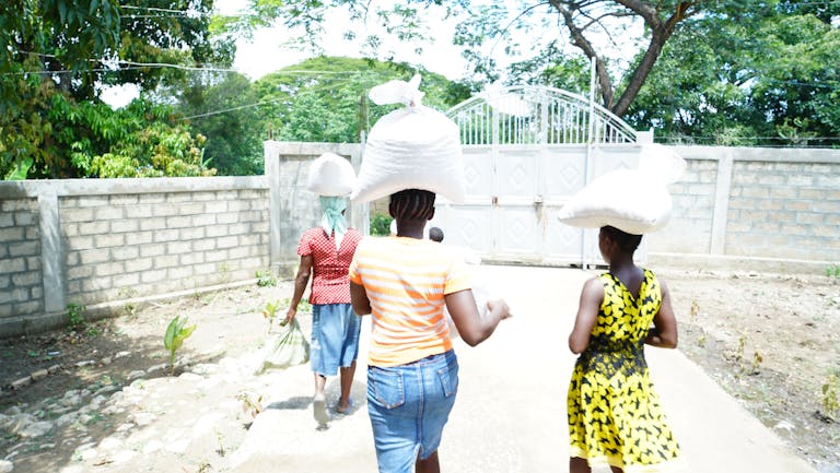 three women walking away from the camera carrying bags of relief food