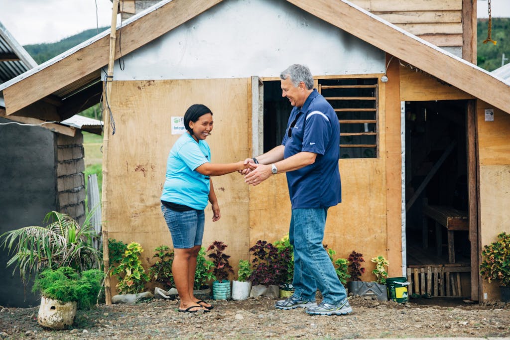 CEO/President Gary Edmonds shakes the hand of a woman outside a wooden house in the Philippines