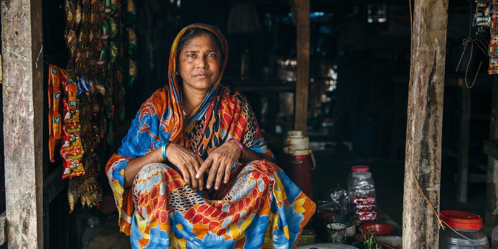 Somber woman in Bangladesh sits in the doorway of a shop wearinga traditional, colorful blue and red sari