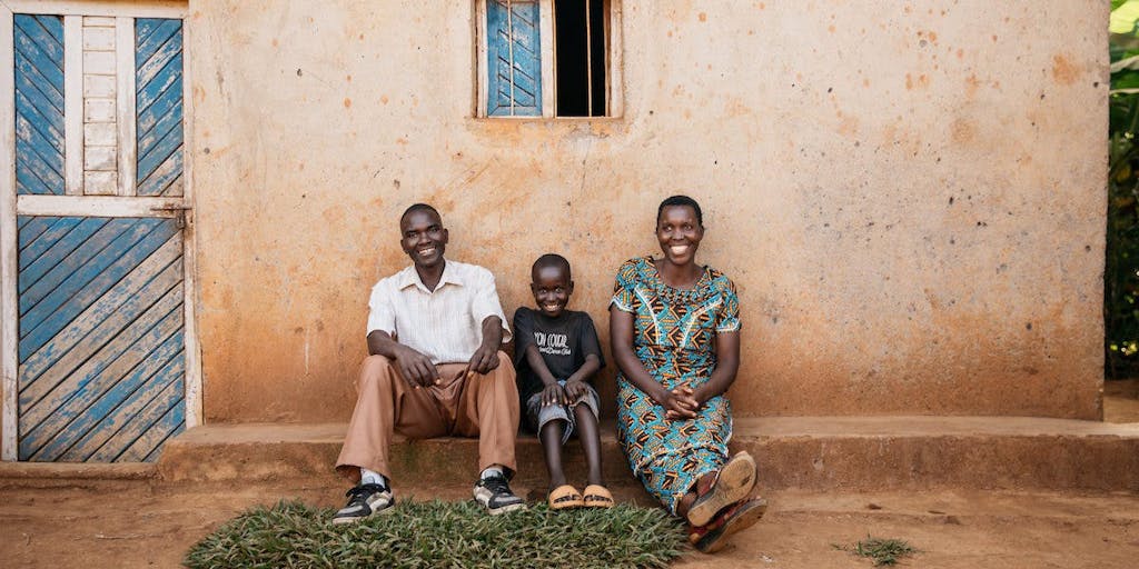 Happy family of father, mother, and son sit outside their house in Burundi, smiling after being healed from deworming treatments.