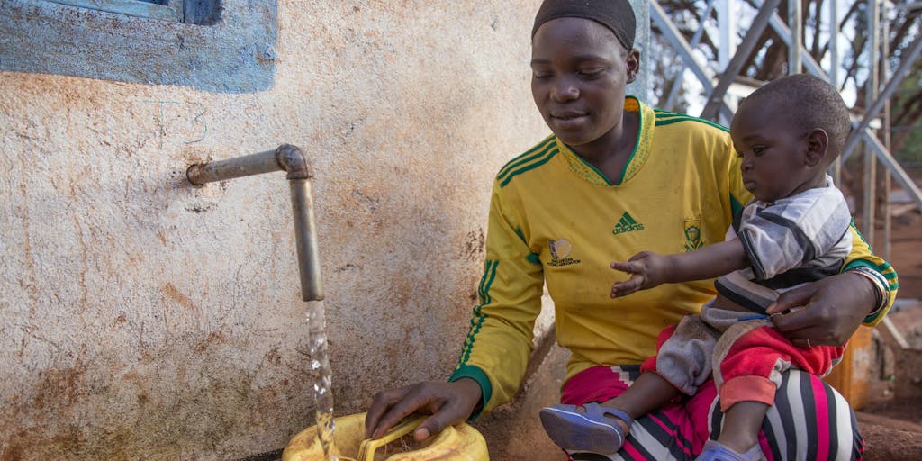 Kenyan mother holding her young boy fills up a jerrycan at a water kiosk for clean water in Marsabit county.