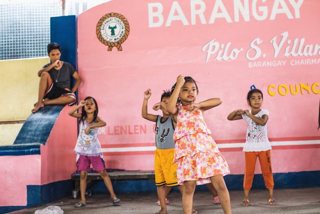 Children in the Philippines dance in a childrens club, with a bright pink wall behind them