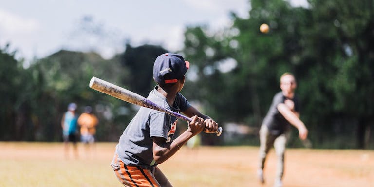 A young boy in the Dominican Republic holds a baseball bat, ready to hit the incoming ball.