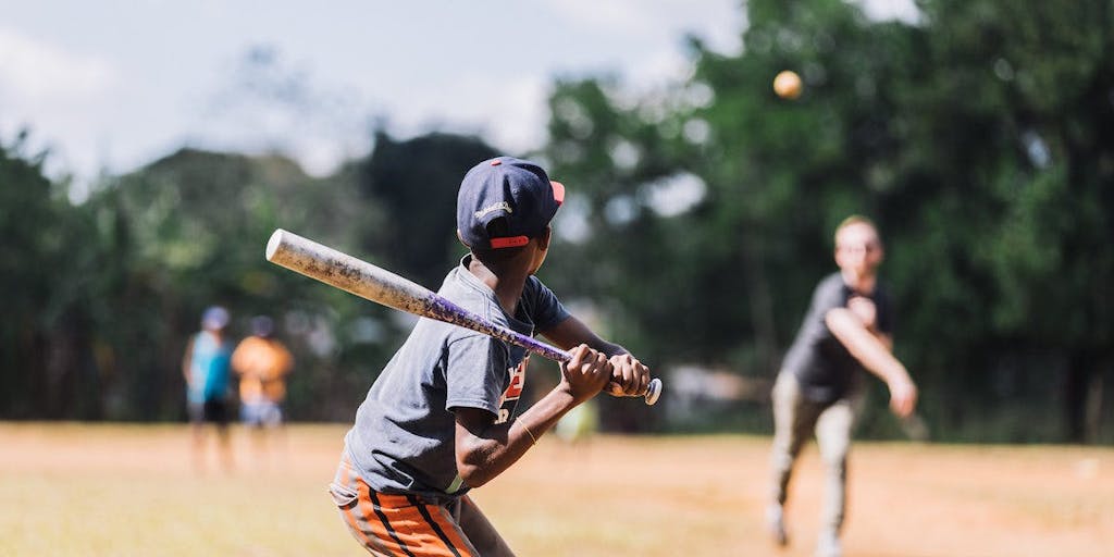 A young boy in the Dominican Republic holds a baseball bat, ready to hit the incoming ball.