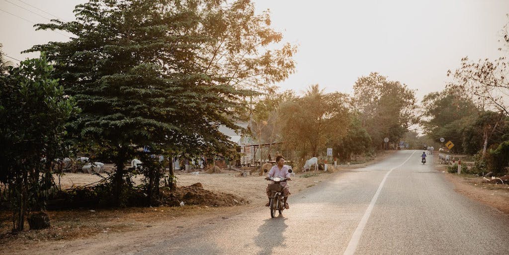 Man in Cambodia travels down the road with motorcycle at sunset