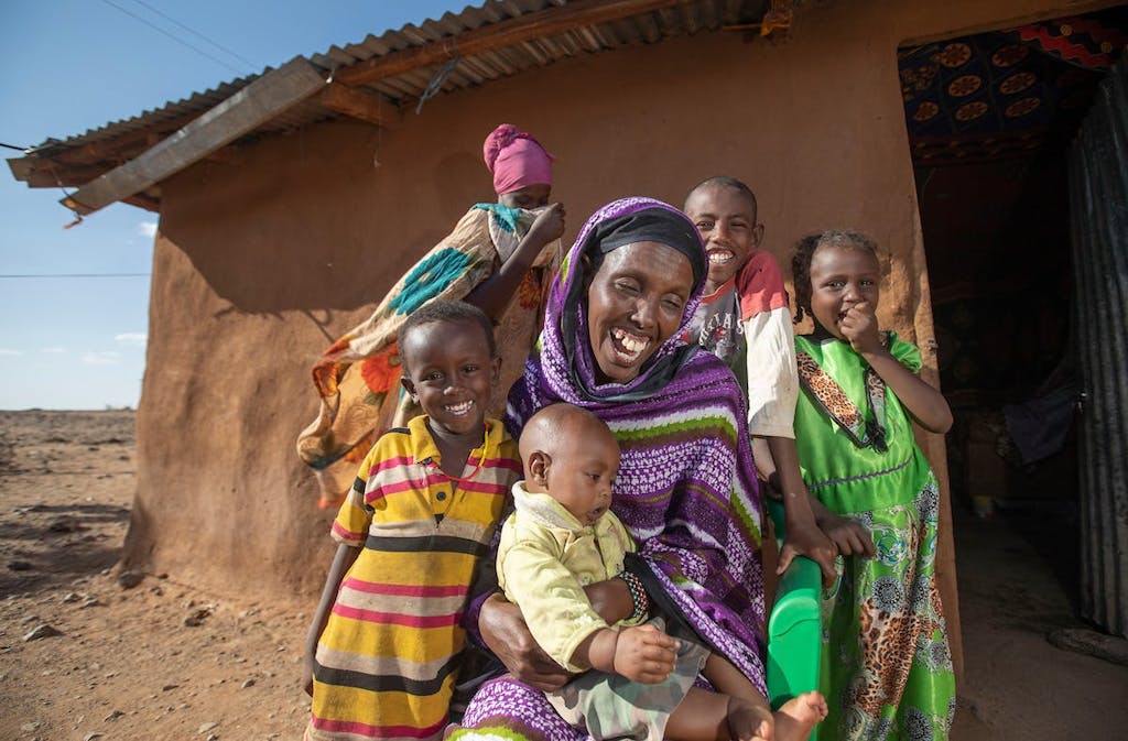 Mother and children laughing in front of their mud brick home