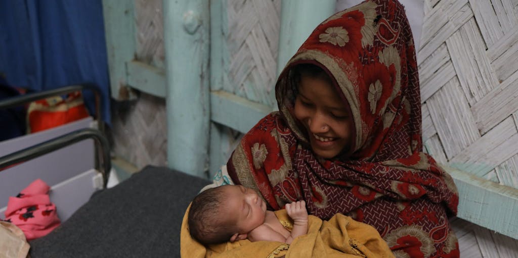 Rohingya refugee mother in headscarf holds her new baby, born in the Kutapalong refugee camp in 2019.
